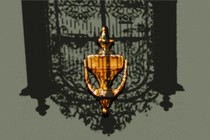 A historic door knocker under the inverted shadow of a historic gate