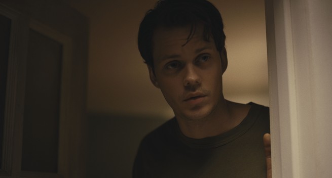 Bill Skarsgård peering around a door in "Barbarian"