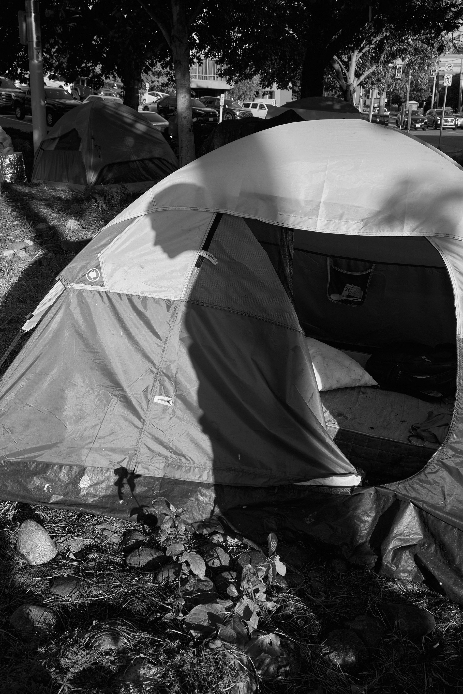 black-and-white photo of tent in homeless camp with shadow of person's profile cast across it