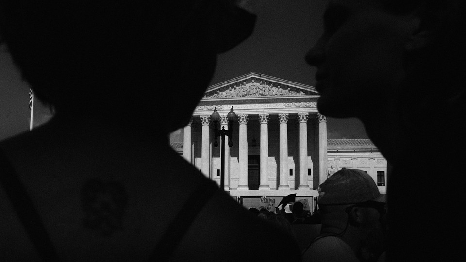 A black-and-white photo of a protester silhouetted in front of the U.S. Supreme Court