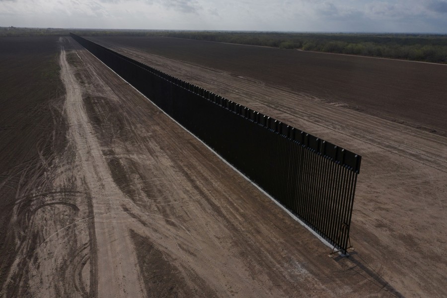 An unfinished stretch of border wall stands in an empty landscape, seen from the air.