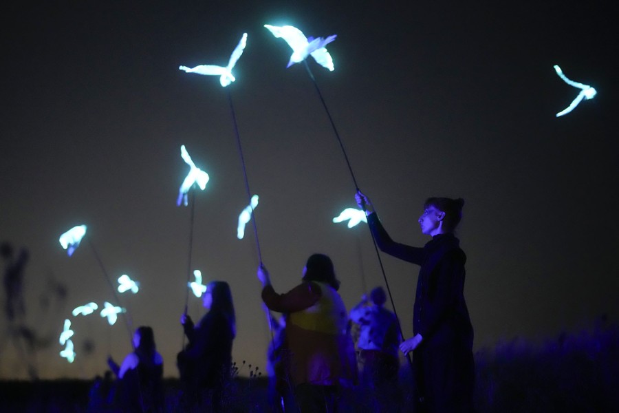 Performers hold illuminated bird sculptures on rods above their heads.