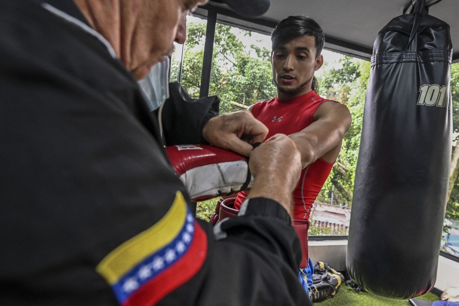 A boxer has his glove adjusted by a trainer inside a gym.