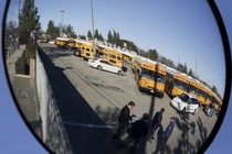 A parking lot filled with school buses is reflected in a bus mirror 