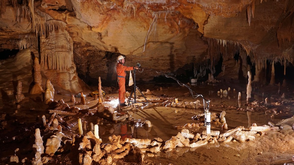 A researcher wearing an orange jumpsuit and a white hard hat in an underground cave