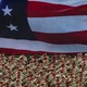 This photo shows a wide shot of U.S. army members saluting and wearing fatigues and matching red berets. Behind them is the image of the American flag