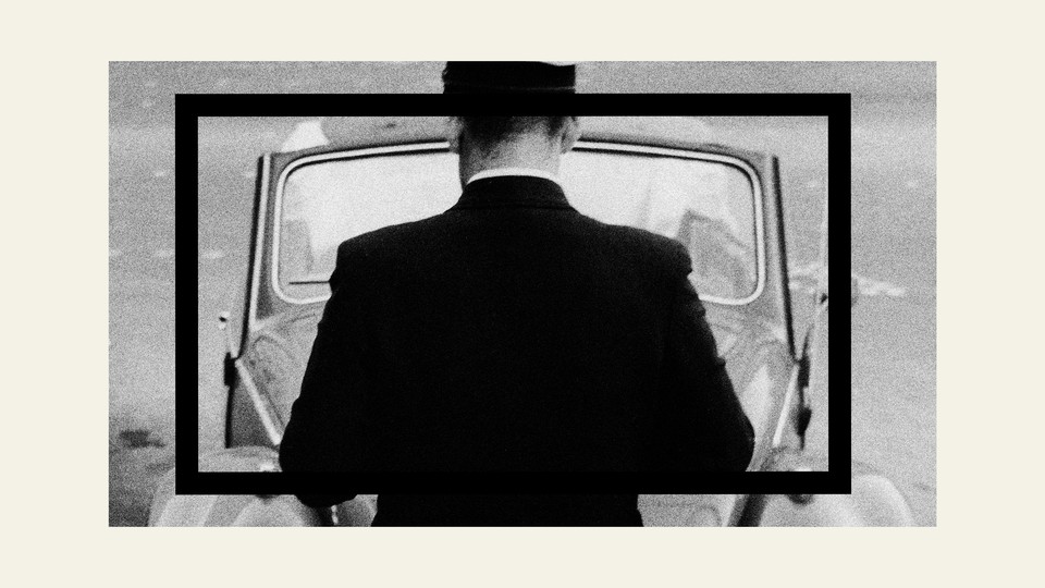 A black-and-white image of a man facing the front of a car