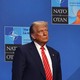 Trump stands alone at a NATO summit in front of a blue background