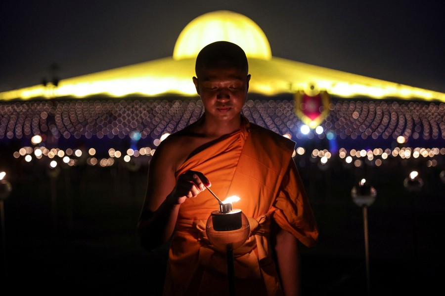 A Buddhist monk lights a candle outside a brightly lit temple.