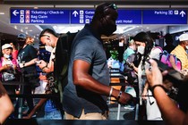 A man with a face mask stands in line at a crowded airport.