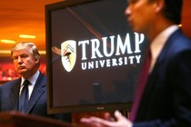 Donald Trump stands next to a screen that reads "Trump University."