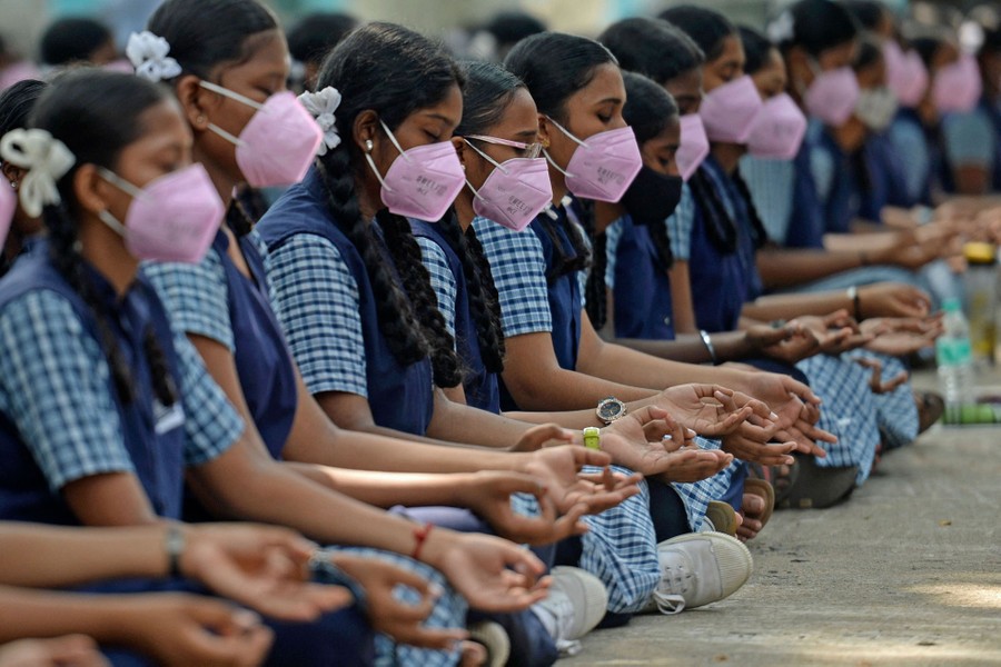 A line of students seated on the ground, meditating, all wearing school uniforms and face masks