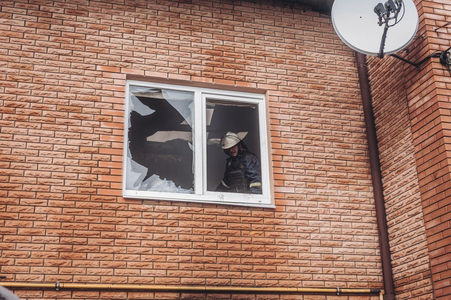 A firefighter at the broken windows of a damaged building.