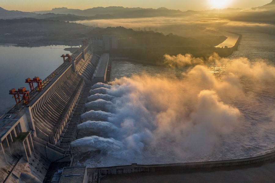 An aerial view of a lot of water shooting out of large spillways in a huge dam