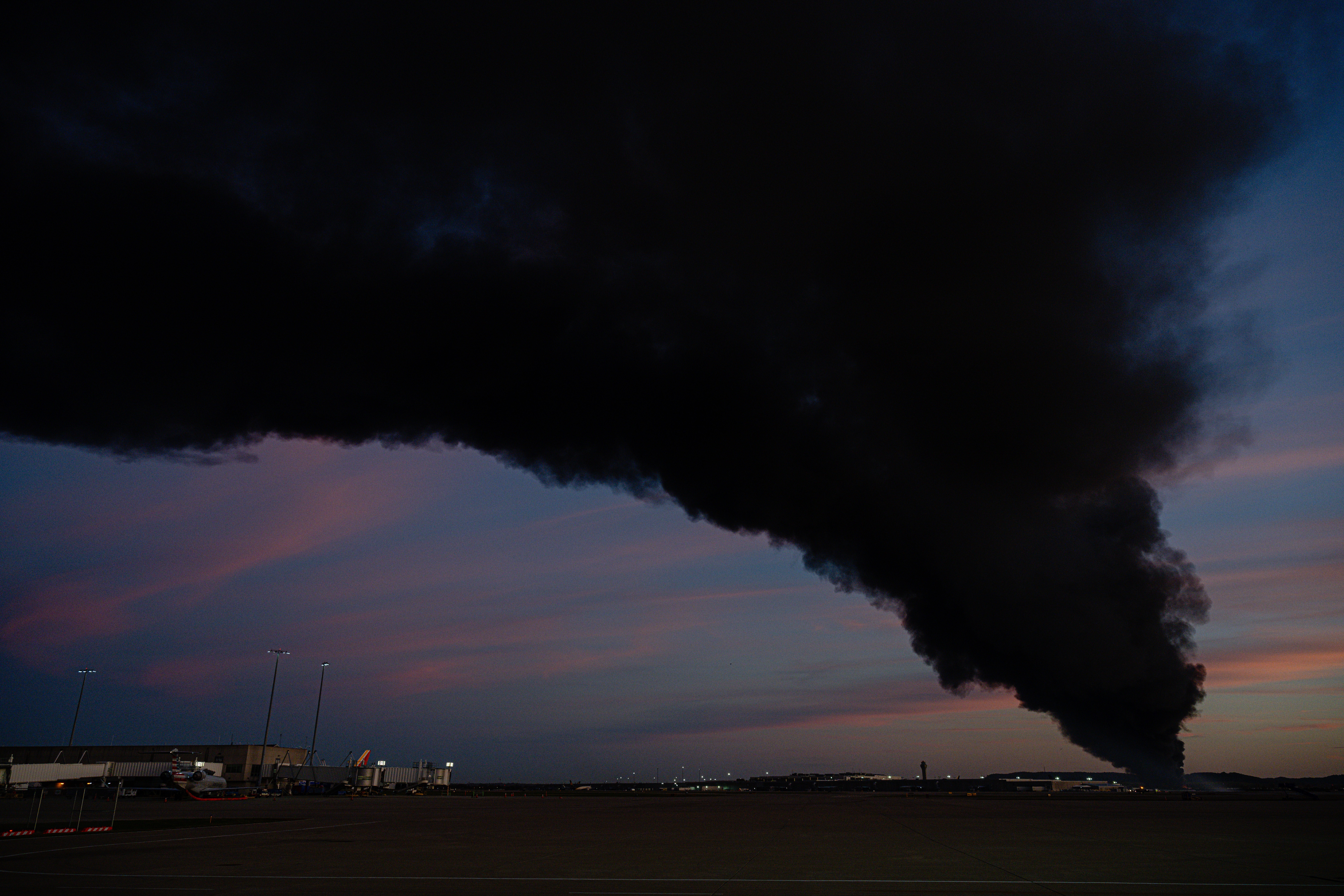 A plume of smoke rises over airport property after a plane crash.