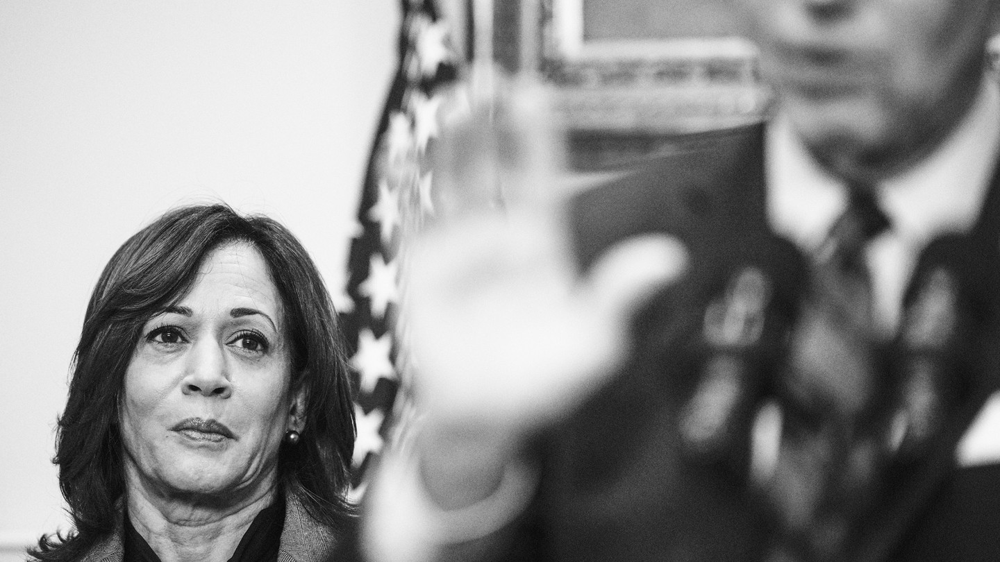 Black-and-white image of Kamala Harris looking at Joe Biden as he speaks in the foreground, his image blurred