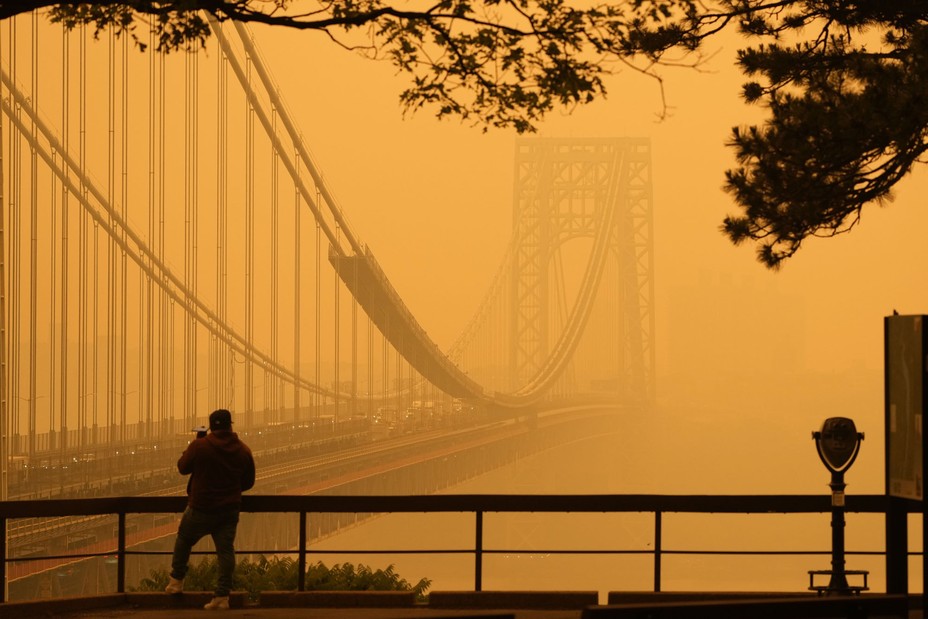 A person stands near a huge suspension bridge that vanishes into an orangish haze.