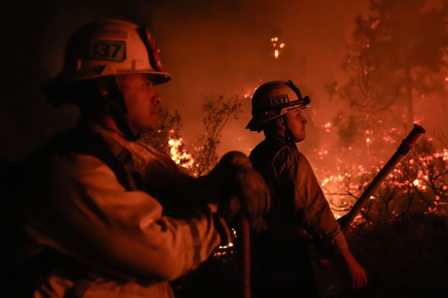Firefighters are illuminated by the glow of a wildfire at night.