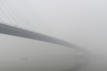 A bridge stretches over a wide river in India in thick fog.