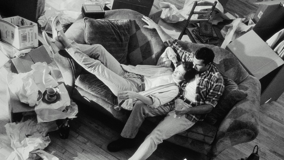 A woman and man cuddle on a couch in a messy room