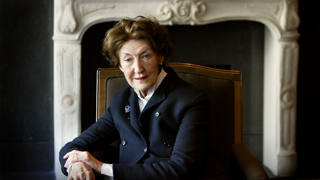 woman in navy double-breasted blazer sits in chair with carved marble fireplace mantel in background