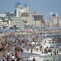 People and beach umbrellas pack the shores of Ocean City, Maryland. Hotels and other buildings also dot the coastline.