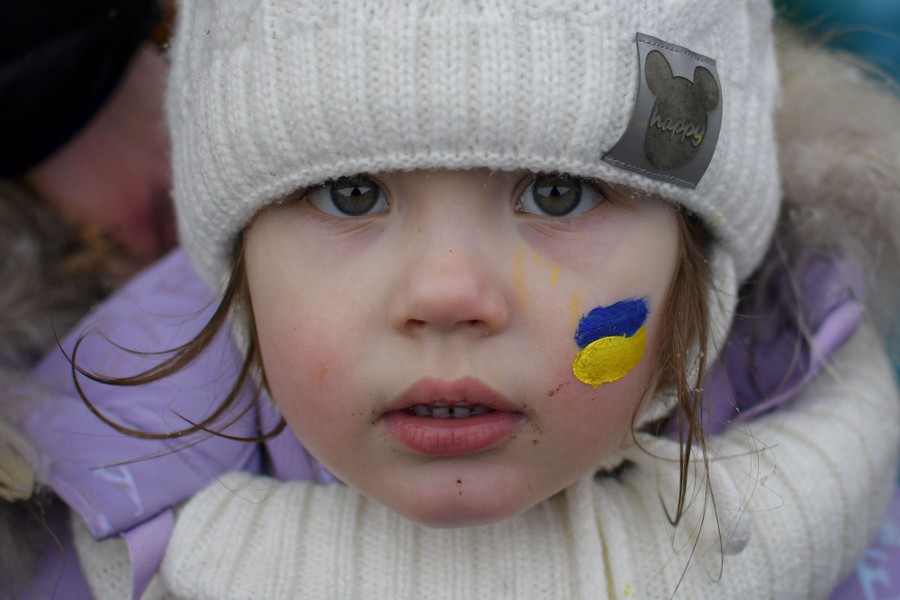 A portrait of a young child wearing winter clothing, with a small patch of blue-and-yellow face paint on their cheek.