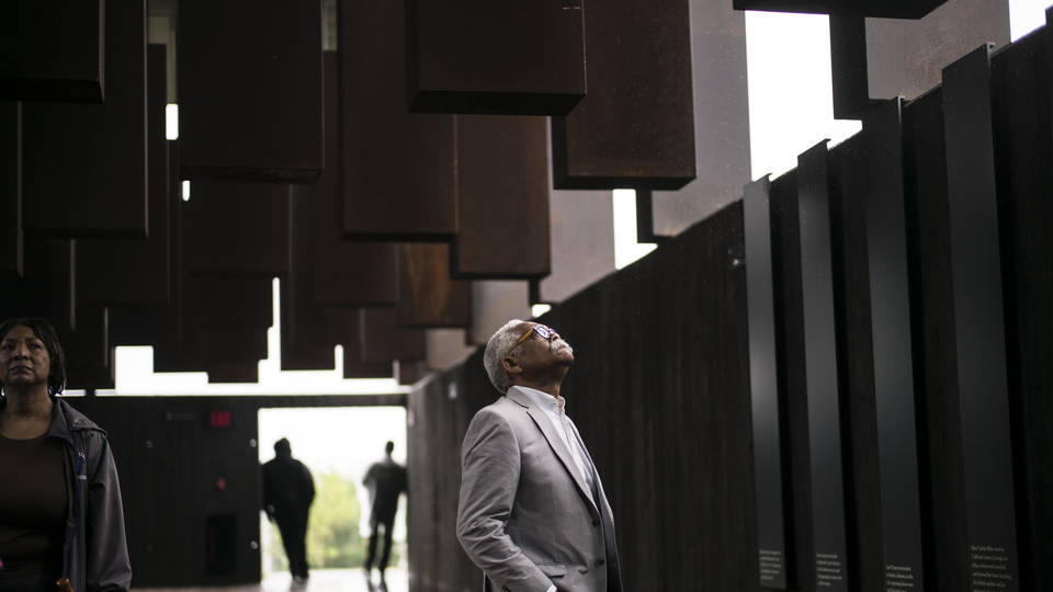 A color photograph of a man looking up at the artwork on the ceiling of the National Memorial for Peace and Justice