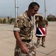 An Iraqi policeman walks past two British military officers, one folding the Union Jack.