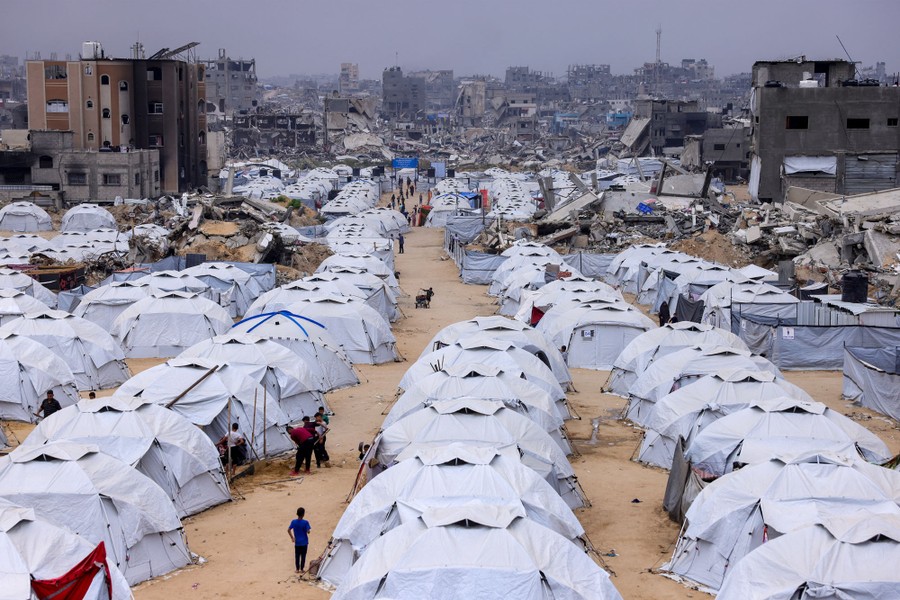 People walk amid rows of tents set up next to the rubble of destroyed buildings in a camp for displaced Palestinians.