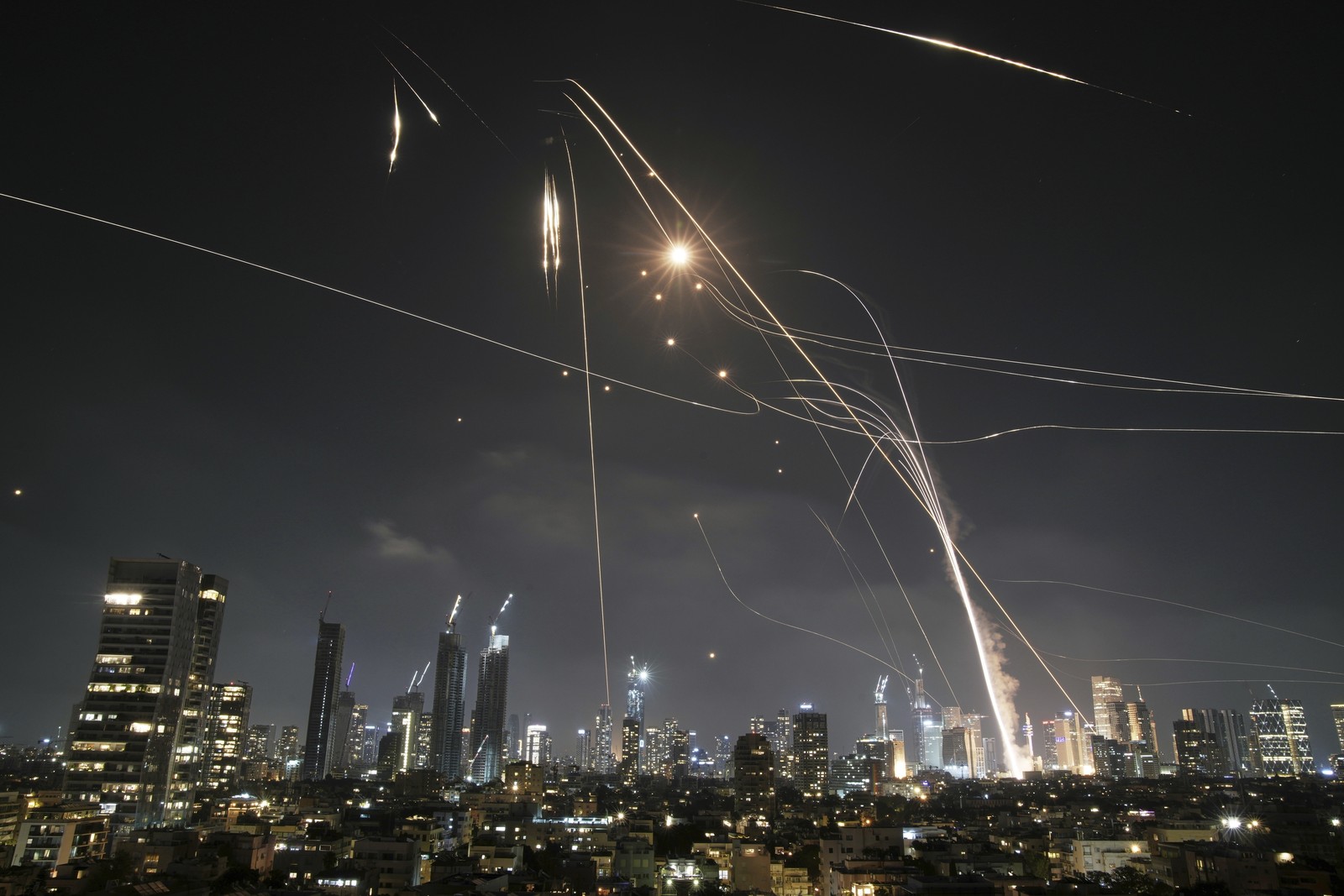 Light streaks are left in the sky above a city at night, as incoming missiles are met by defensive missiles.