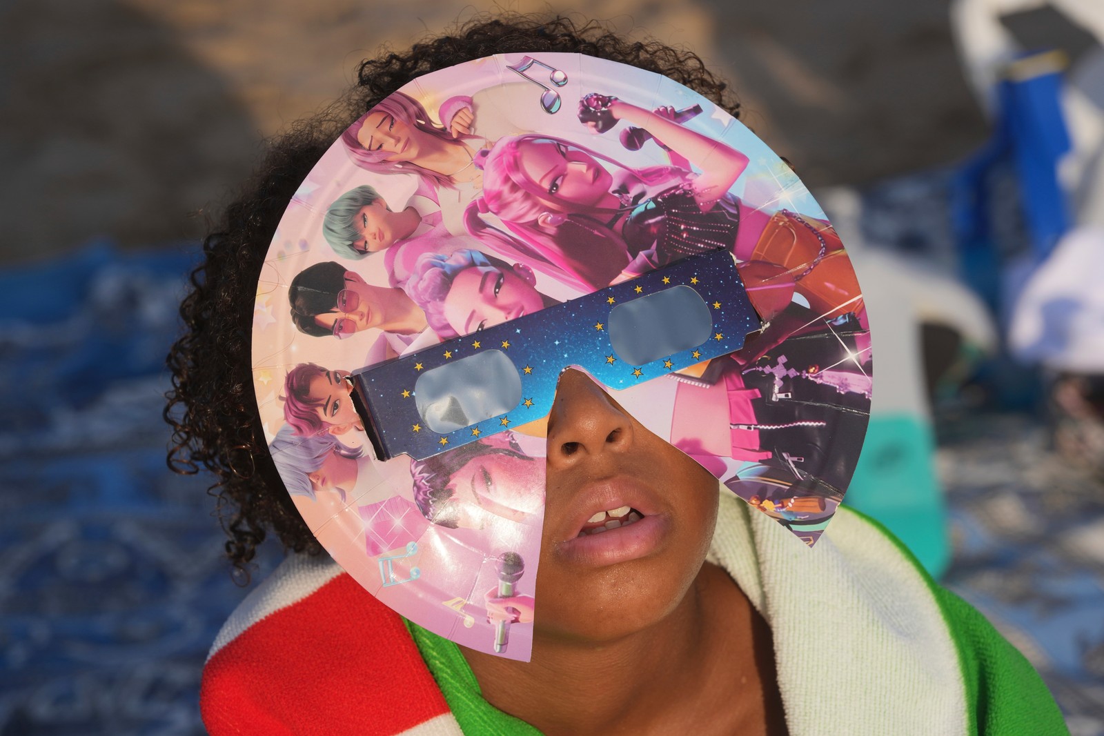 A young person wears special eclipse glasses decorated with 'K-Pop Demon Hunters' characters.