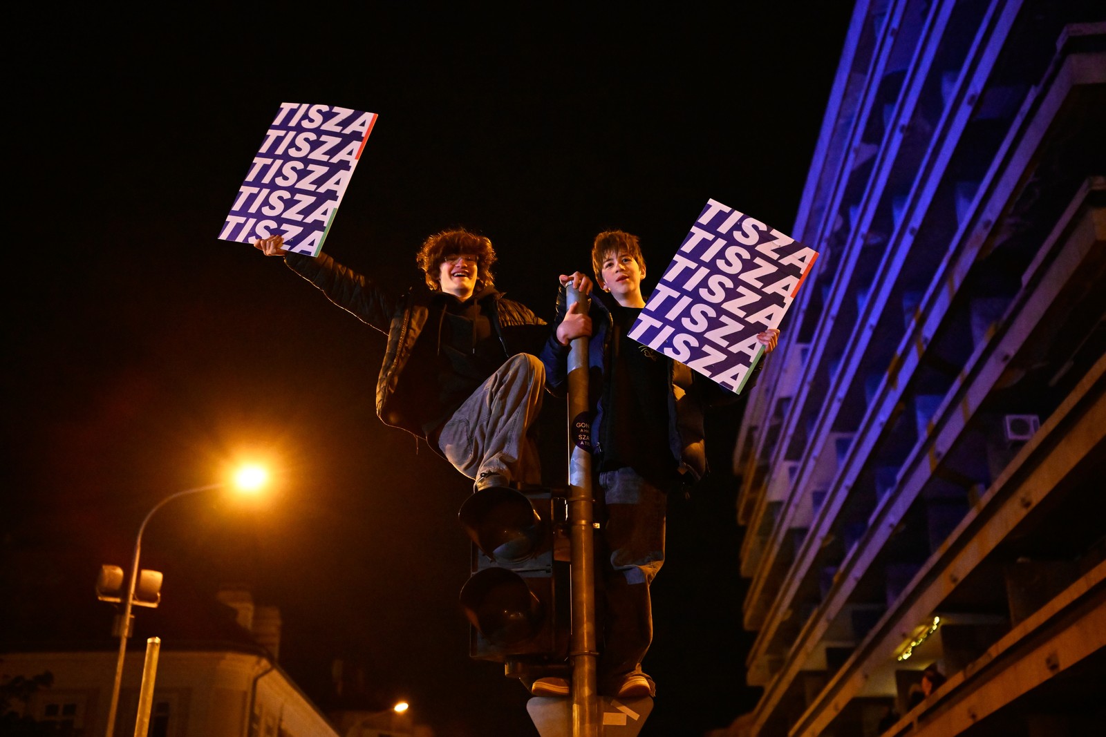 Two supporters hang from a traffic light post, holding signs that read 