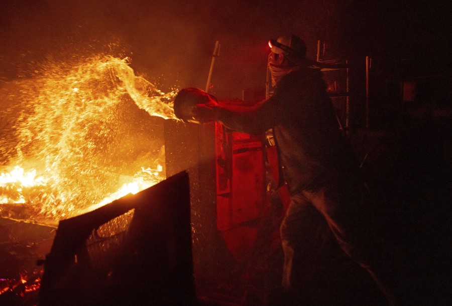 A person throws a bucket of water onto an approaching fire.
