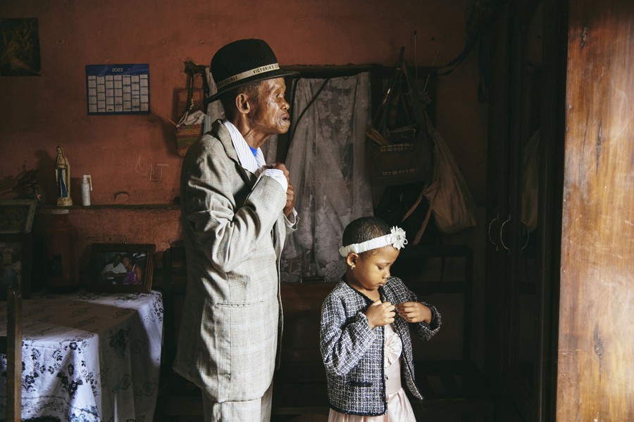 A grandfather and granddaughter adjust their clothing in a room while preparing to go to church.