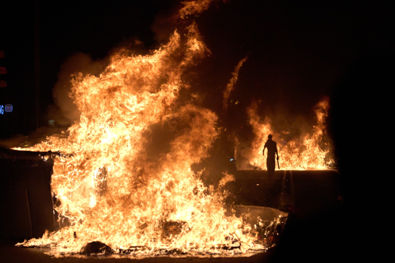 A demonstrator walks past burning trash cans during a protest.