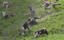 Eight men are seen tumbling and trying to run down a very steep hill.