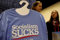 A T-shirt on a hanger reads "Socialism Sucks"; two young women stand behind it.