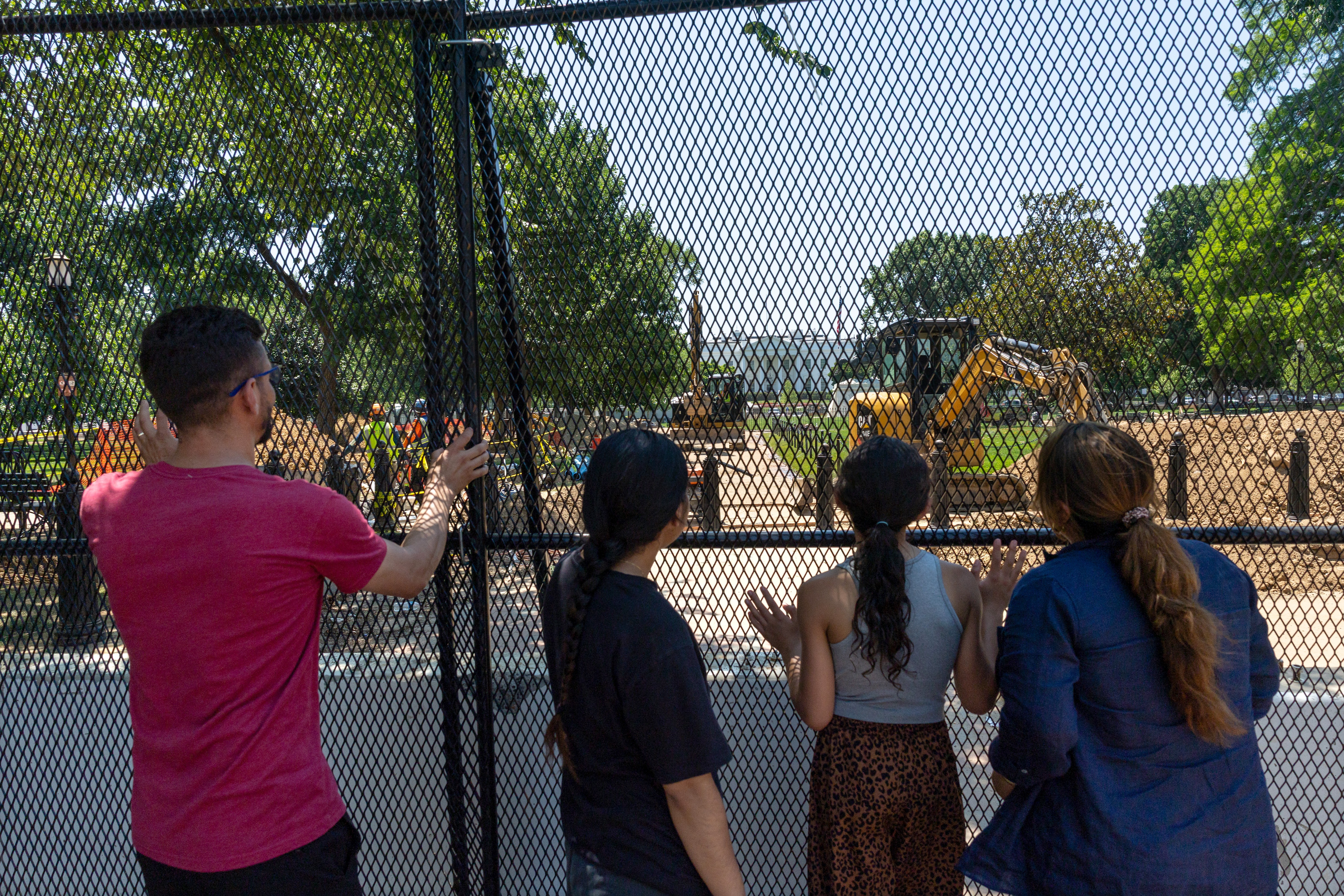A family of four looks through fencing at ongoing construction at the White House.