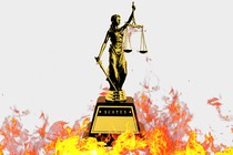 A statue of lady justice is surrounded by flames.