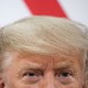 Top half of President Donald Trump's head in front of red and white stripes of the American flag