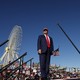 Donald Trump stands on stage at a rally with a giant ferris wheel and crane behind him