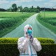 Photo of a Chinese health worker in a protective suit, against a backdrop picture of a country road