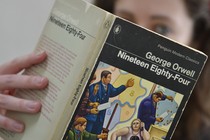 A woman, who's blurred out, holds a copy of George Orwell's '1984'