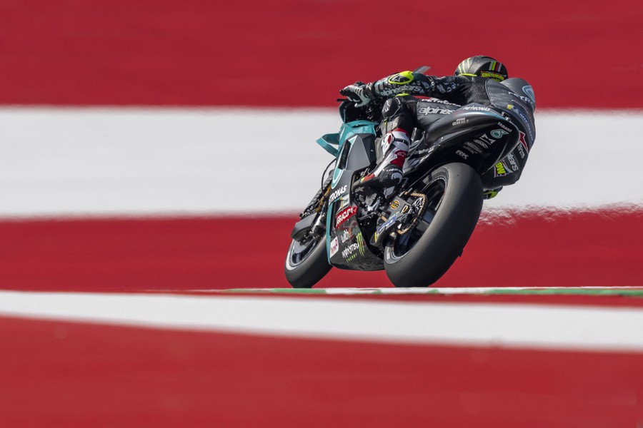 A motorcycle racer rides on a road lined with red and white stripes.