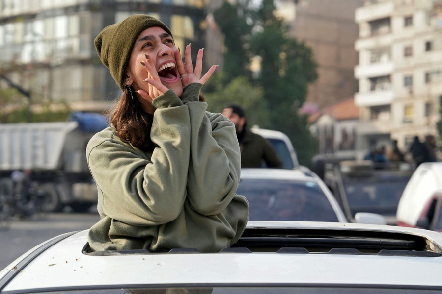 A woman shouts while standing in the open sunroof of a car.