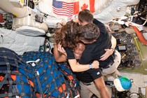 Four astronauts hug while inside a capsule, floating in micro-gravity.