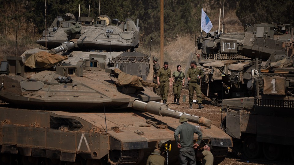 Israeli soldiers stand and walk among tanks and armored personnel carriers.