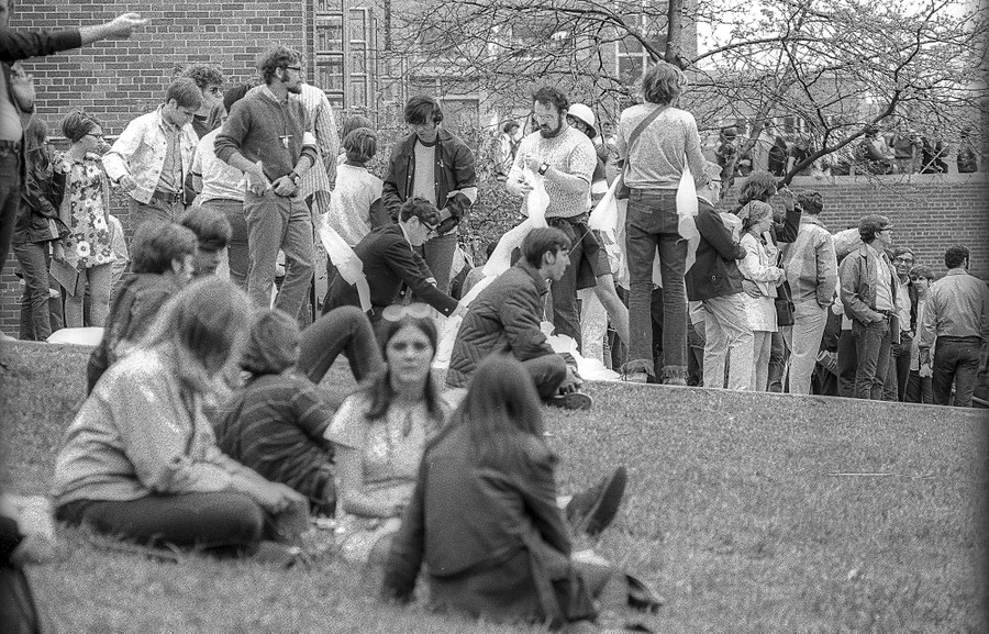 A crowd of student protesters gathers at the top of a gentle hill near campus buildings.