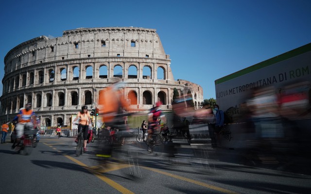 People bike past the remains of the ancient Colosseum in Rome